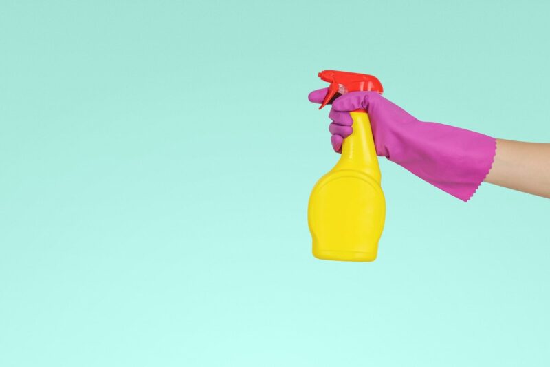 Pink cleaning gloved hand with oil spray bottle