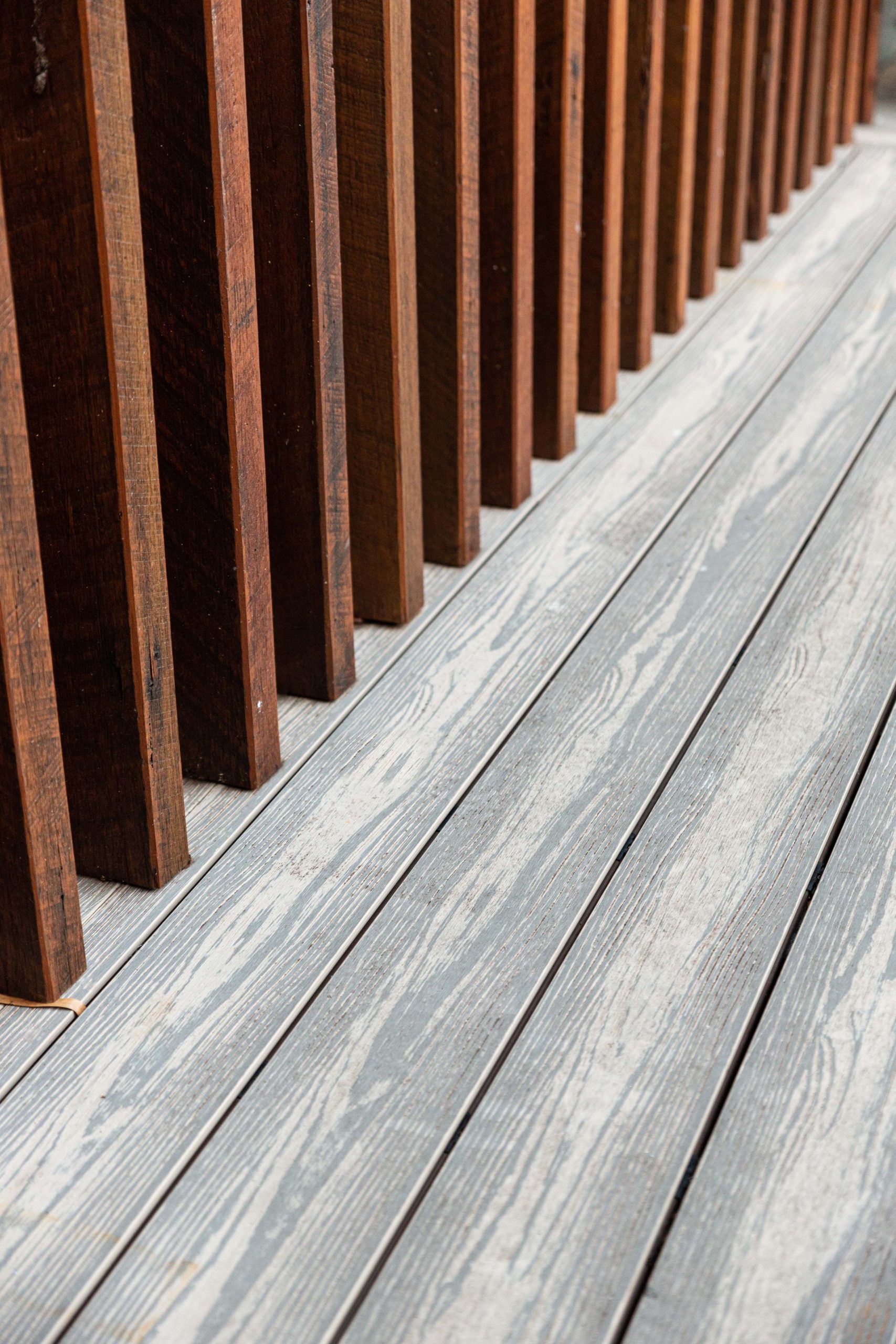 Dark wooden rail posts installed on grey silver composite decking boards