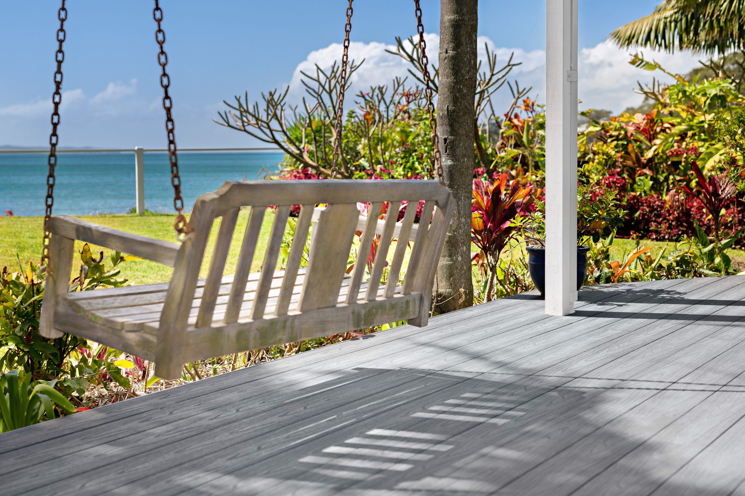 A two person, wooden patio swing overlooking the ocean