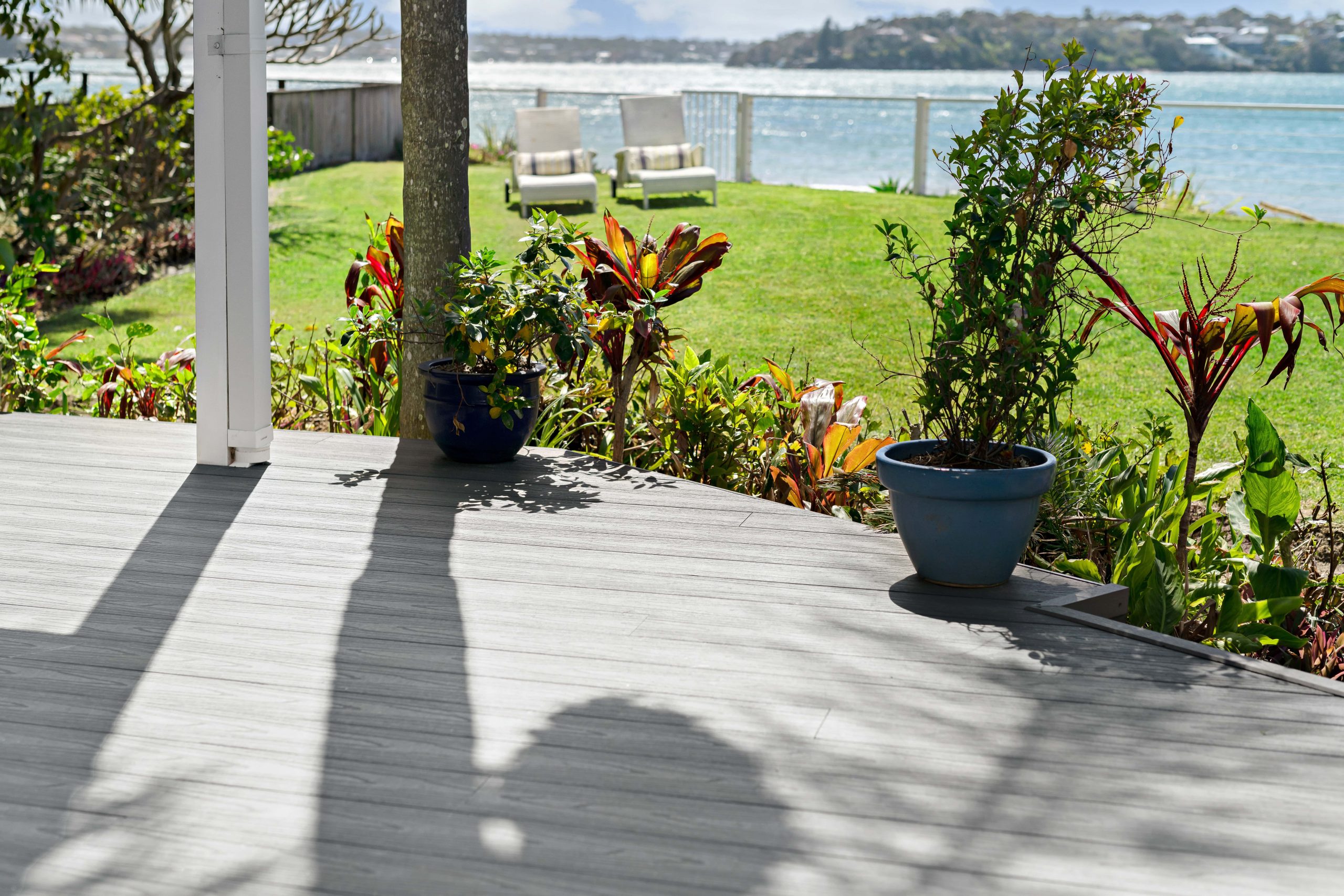 Shadows across gray composite decking boards overlooking a lawn and ocean