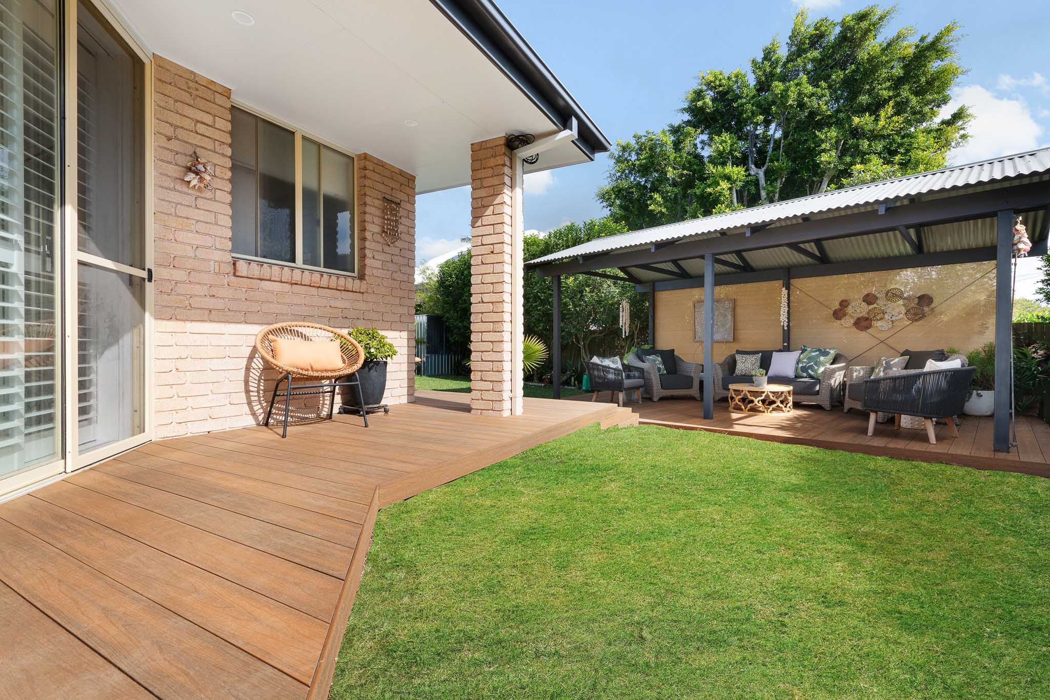 A small section of a patio built with Teak composite decking boards, next to a green lawn