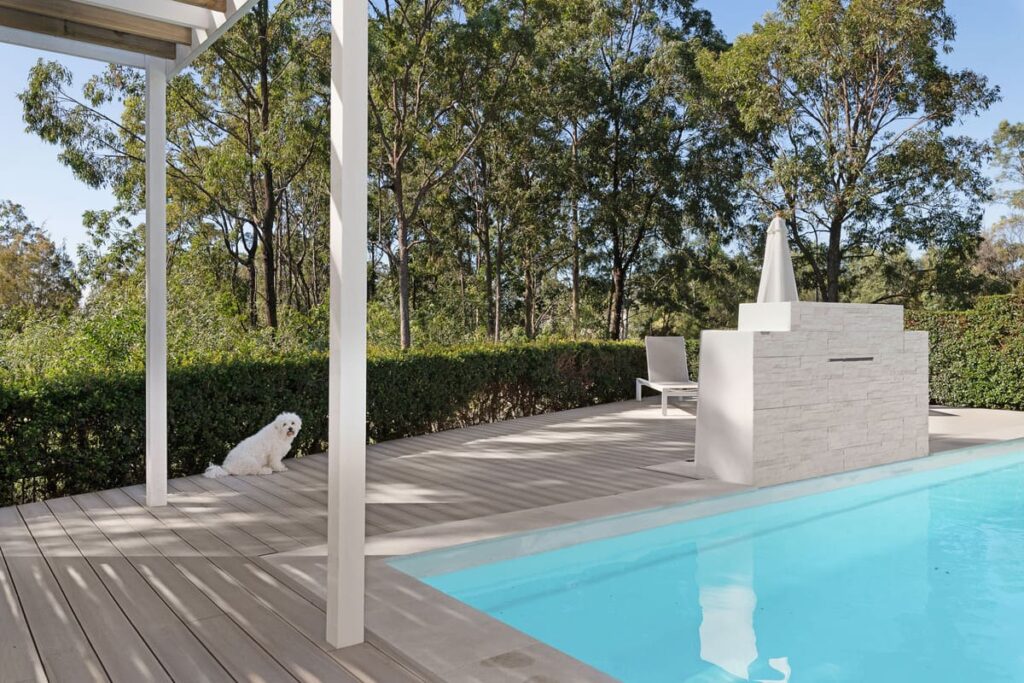 a dog sitting on a composite deck next to a pool