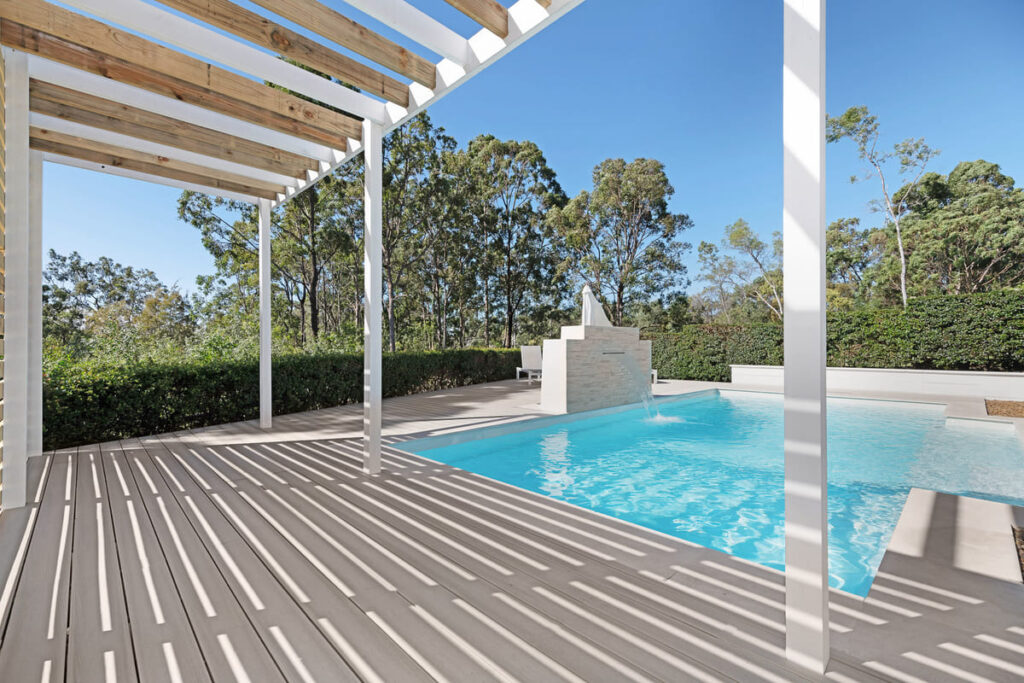 a pool with a wooden deck and a white pergola