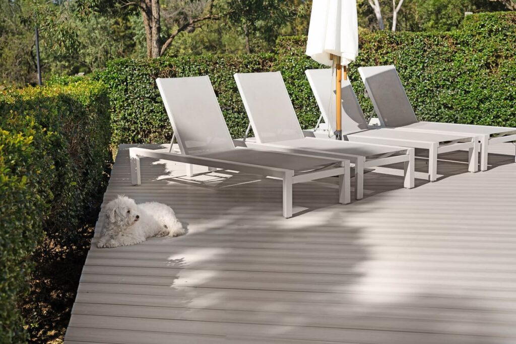 a dog lying on a composite deck with chairs and umbrella
