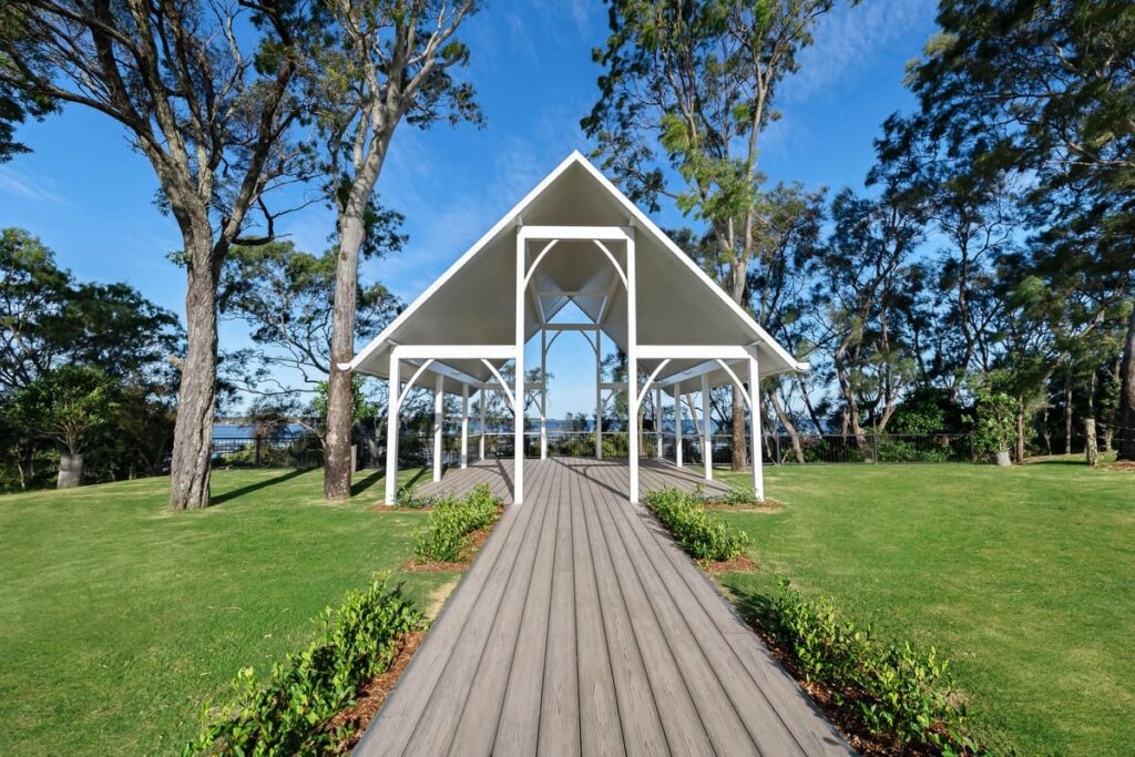 a white structure with a grey composite decking walkway and trees