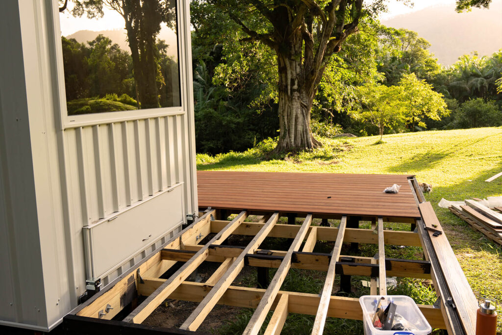 Progress view of a tiny house deck build in Byron Bay, showing Titanium Tawny composite decking partially installed over a timber frame with sunset light across the landscape