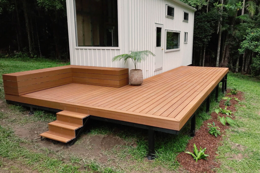 Completed DIY composite decking beside a tiny house in Byron Bay, featuring Titanium Tawny boards, built-in seating, and landscaped garden edging.