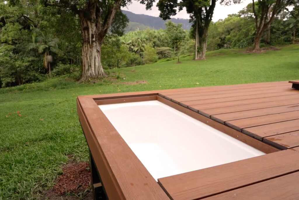Hidden bathtub built into Titanium Tawny composite decking in a lush Byron Bay landscape, showcasing a unique DIY tiny house outdoor feature.
