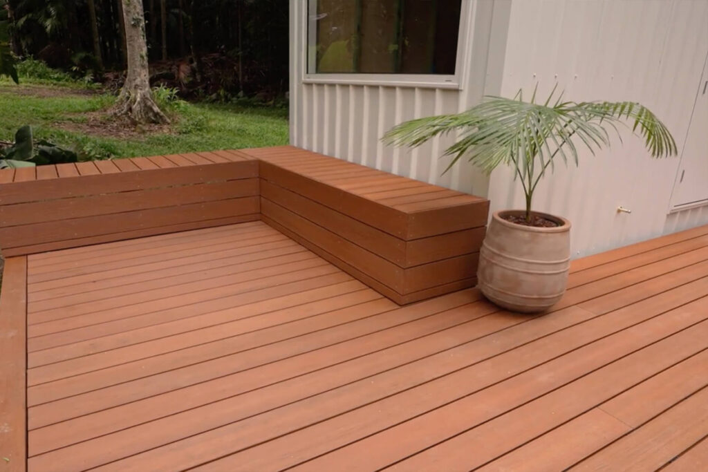 Built-in composite bench seating on Titanium Tawny decking beside a tiny house in Byron Bay, with a potted palm adding a relaxed outdoor touch.