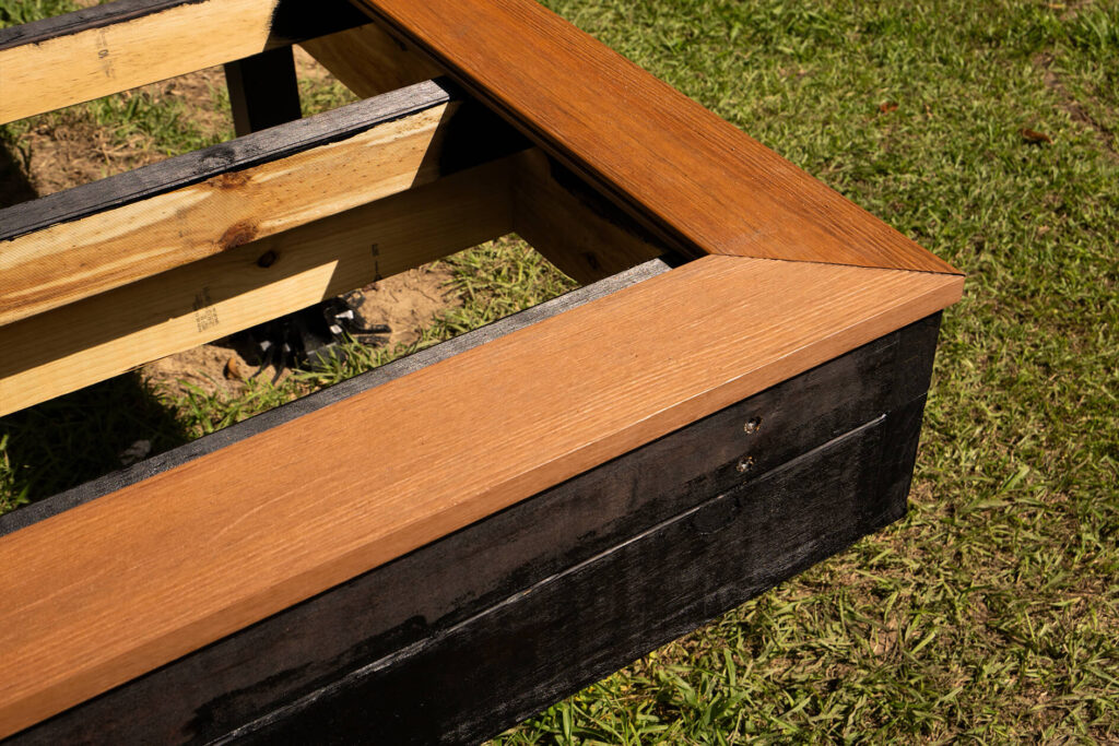 Close-up of DIY composite decking mitre joint detail in a tiny house build in Byron Bay, showing precise installation over a treated timber and black-framed substructure.
