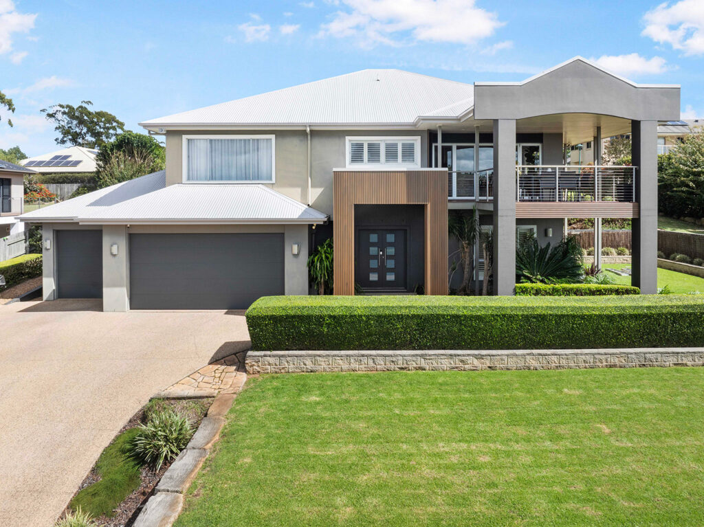 Modern two-story home with Country Teak composite cladding at the entry, triple garage, balcony, and manicured landscaping.