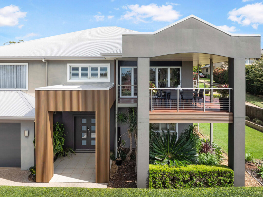 Front view of a stylish home with Country Teak composite cladding entry, tiled porch, balcony with cable railing, and lush greenery.