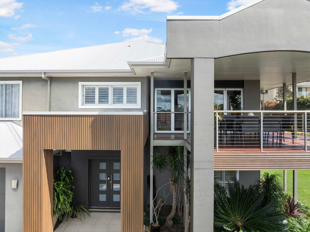 Front entrance with Country Teak composite cladding, double door entry, tiled porch, and balcony with stainless steel railing.